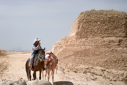 cairo, Egypt – October 26, 2023: A solitary man on horseback stands in the desert, overlooking the ruins of a bygone era.