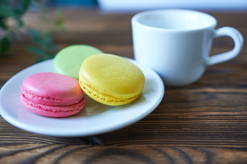 Colorful macaroons on a plate and a cup of coffee on a wooden table.