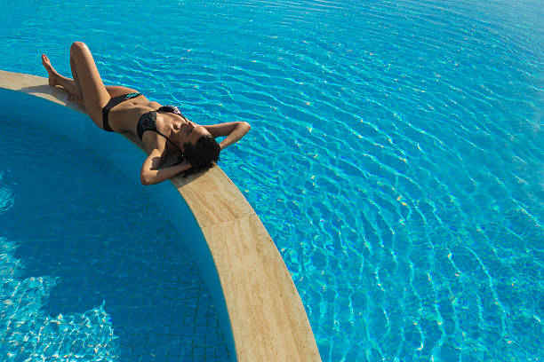 istock Young woman sunbathing by pool 181992467