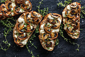 Mushroom toasts with cheese and fresh thyme on a black background, close-up