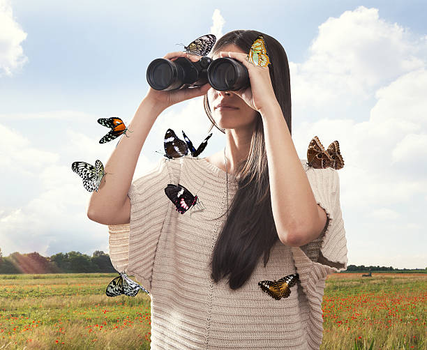 Jovem mulher assistindo com binocular coberto de borboletas - foto de acervo