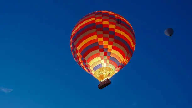 Photo of A multicolored hot air balloon with people in the basket, against the dark sky at dawn. Fire burns inside.