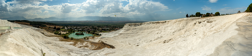 A panorama from above of the white travertines in Pamukkale and the lake at their base.