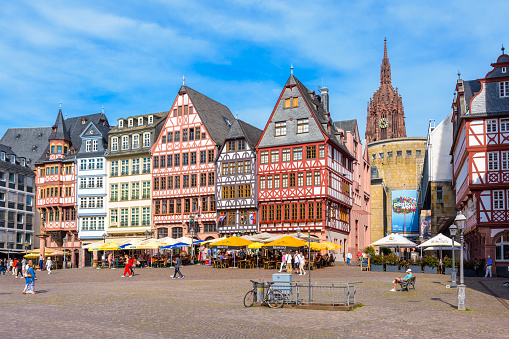 Frankfurt, Germany - Aug. 17, 2023: Tourists stroll on the Römerberg square in the old town, lined with sidewalk cafes and colorful half-timbered houses, overlooked by the steeple of the cathedral.