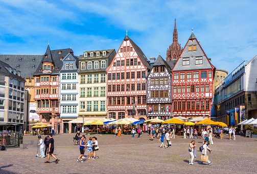Frankfurt, Germany - Aug. 17, 2023: Tourists stroll on the Römerberg square in the old town, lined with sidewalk cafes and colorful half-timbered houses, overlooked by the steeple of the cathedral.