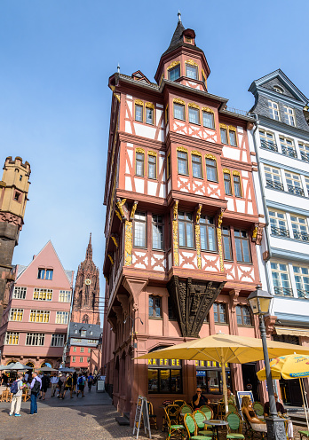 Frankfurt am Main, Germany - August 17, 2023: Steeple of the cathedral seen from the Römerberg square in the old town, lined with colorful half-timbered houses.