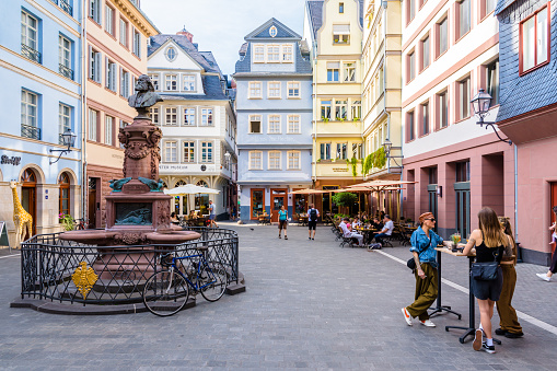 Frankfurt am Main, Germany - Aug. 17, 2023: The Stoltze fountain, dedicated to poet Friedrich Stoltze, stands on the Chicken Market square lined with colorful houses from the 17th and 18th centuries.