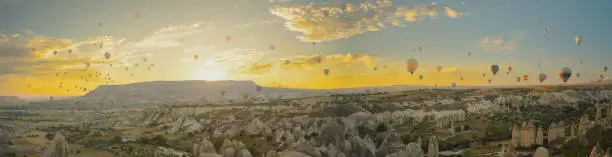 Photo of A vast number of hot air balloons in Cappadocia, with the sun about to rise behind the mountains. Golden clouds create a breathtaking panorama.