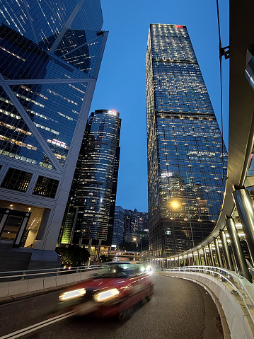 Taxi riding on an elevated road by the Cheung Kong Centre skyscraper at night in Hong Kong Admiralty district.