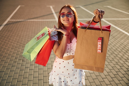 Showing shopping bag with sale stickers on it. Beautiful woman in casual clothes is outdoors.