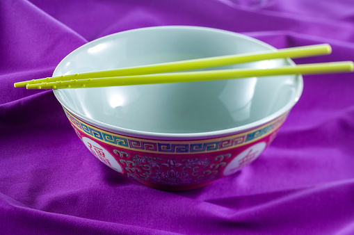 Empty Chinese noodles bowl with chopsticks on a purple background.