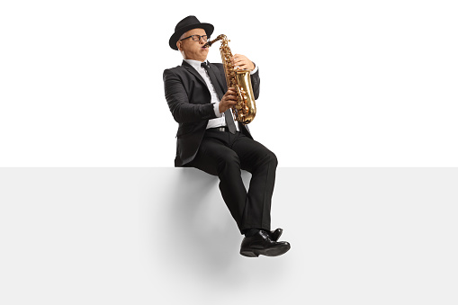 Mature male artist playing a saxophone seated on a blank banner isolated on white background