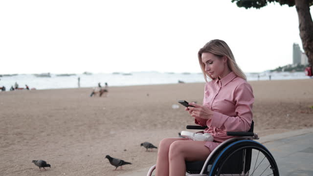 Accessible Travel: Disabled Woman in Wheelchair Relishes Scenic Beauty of Pattaya Beach - Enjoying Coastal View and Mobile Photography