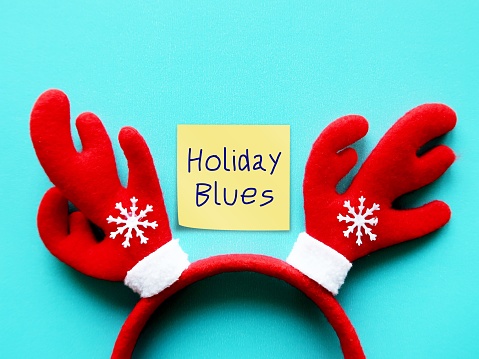 Reindeer headband on blue copy space background with note written Holiday Blues -  refers to feelings of sadness that occur during Christmas festive seaso - feelings of anxiety, depression, sadness, loneliness or negative emotions