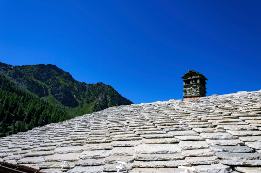Italy, Aosta Valley, Cuneaz, stone roof and chimney in foreground with blu sky in background