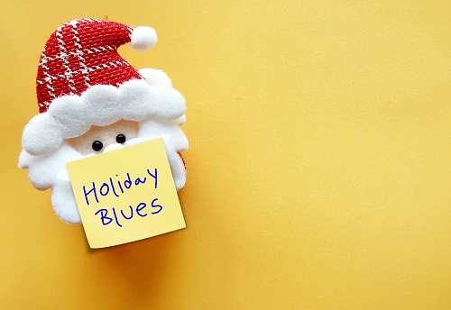 Mini santa on yellow copy space background with note written Holiday Blues -  refers to feelings of sadness that occur during Christmas festive seaso - feelings of anxiety, depression, sadness, loneliness or negative emotions