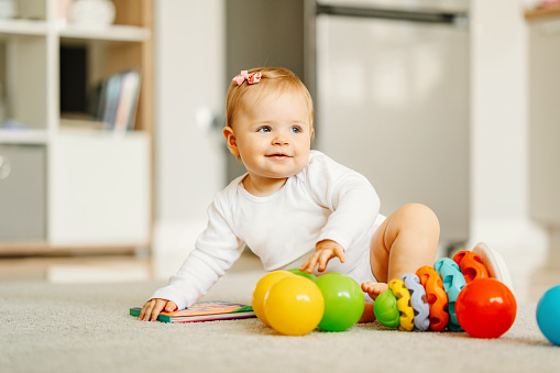 Image of happy baby girl sitting on floor and playing with toys.