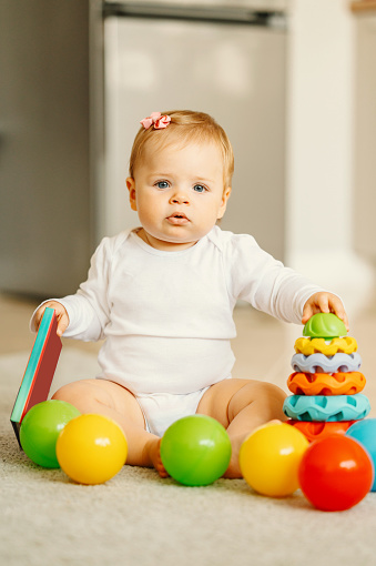 Vertical photo of baby girl sitting on floor with some toys.