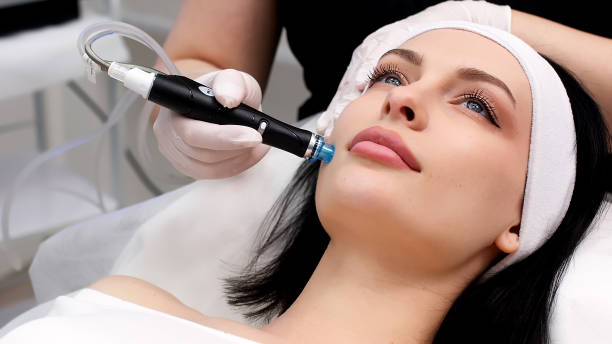 istock Cosmetology clinic. Professional female cosmetologist doing Hydradermabrasian procedure while being a work. Attractive nice woman lying on the medical bed while having beauty procedures 1820029062