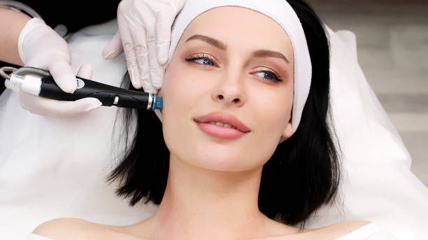 istock Cosmetology clinic. Professional female cosmetologist doing Hydradermabrasian procedure while being a work. Attractive nice woman lying on the medical bed while having beauty procedures 1820029087