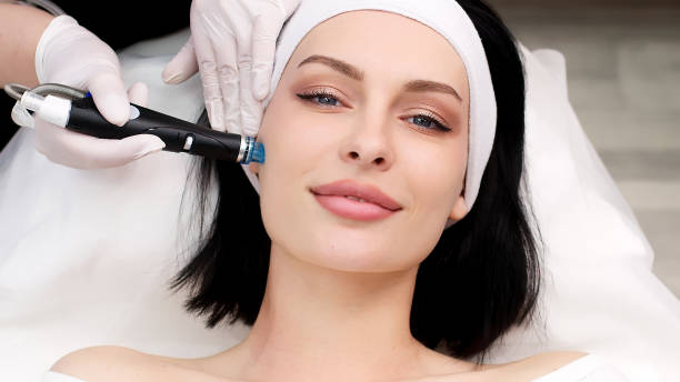 istock Cosmetology clinic. Professional female cosmetologist doing Hydradermabrasian procedure while being a work. Attractive nice woman lying on the medical bed while having beauty procedures 1820029089