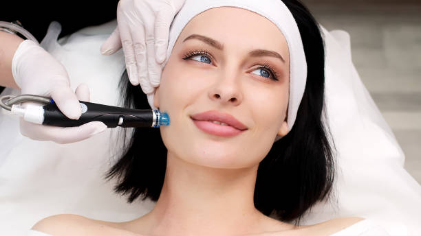 istock Cosmetology clinic. Professional female cosmetologist doing Hydradermabrasian procedure while being a work. Attractive nice woman lying on the medical bed while having beauty procedures 1820029092