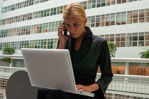 waist up shot of a blond businesswoman in black dress talking on cellphone in office hallway