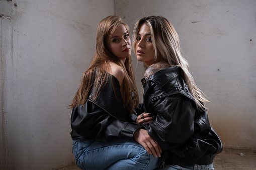 Two young and beautiful blonde women were wearing blue jeans and leather jackets and posing alternatives.