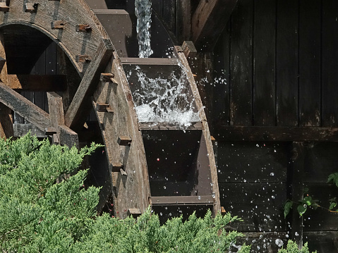 Wusterhausen, Brandenburg - Germany - 06-28-2022: An old mill wheel that no longer works on a house wall and a river made of wood and a mechanism to regulate the flow of water, called weir.