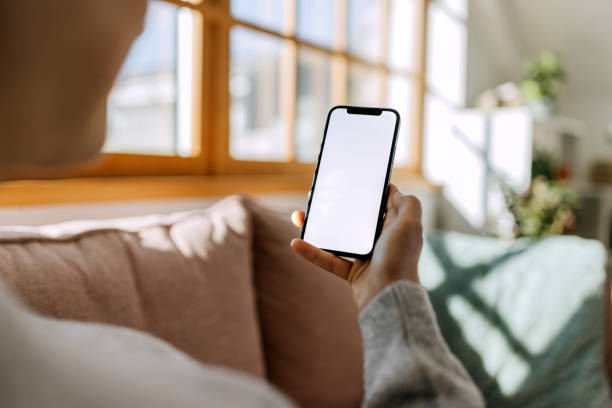 Woman using a smart phone with blank screen Back view close up of a woman hand using a smart phone with blank screen sitting on a couch at home looking at cell phone screen stock pictures, royalty-free photos & images