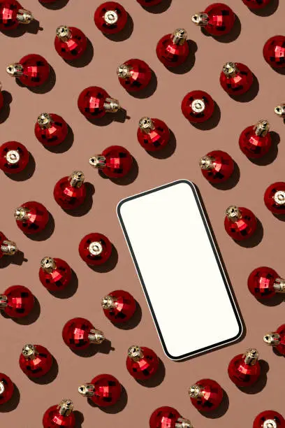Photo of Smartphone mockup with shiny red Christmas balls on brown background.