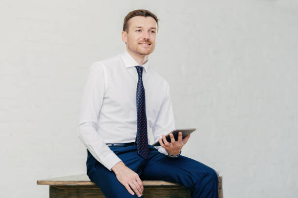 istock Confident professional in a crisp white shirt and tie, casually using a tablet in a bright office 1820100061