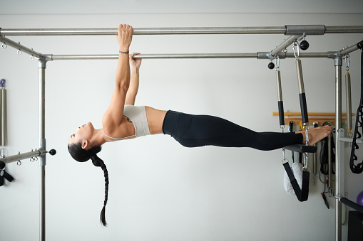 Strong young sportswoman doing upside down pull ups in special machine