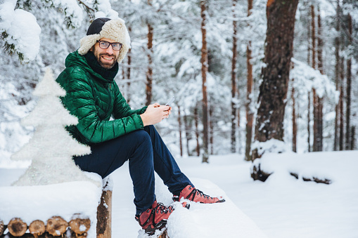 Cheerful man texting on phone, seated on snowy bench in forest