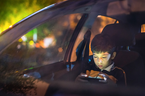 Night scene of a 9 years old boy playing in mobile phone in car cabin.