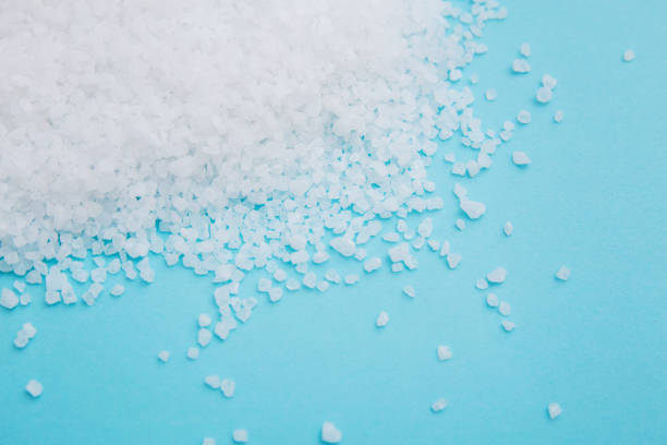 Scattered sea salt on the sky blue paper background. Coarse grinding of edible sea salt close-up. Sodium chloride, maintaining acid-base balance in the body for health.