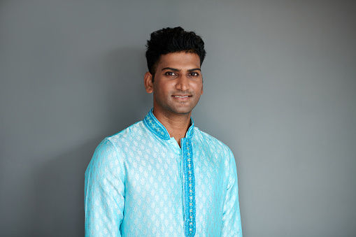 Portrait of positive Indian man in blue kurta standing against grey background