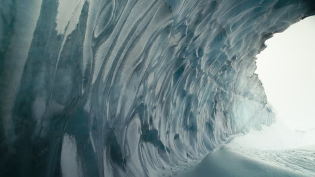 Beautiful blue ice cave tunnel with snow and giant exit slow pan