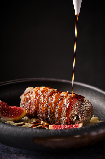 Delicious appetizing piece of pig trotter with pouring fresh sauce placed in plate against dark background