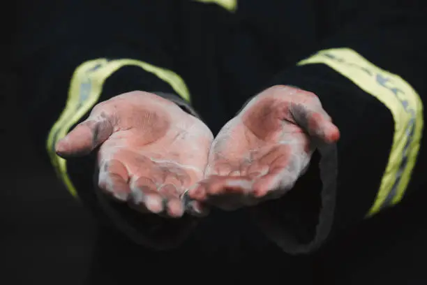 Photo of Help, service and the dirty hands of a firefighter closeup on a dark background for safety or rescue. Ash, dust and the palms of an emergency person in uniform on the scene of an accident or mistake