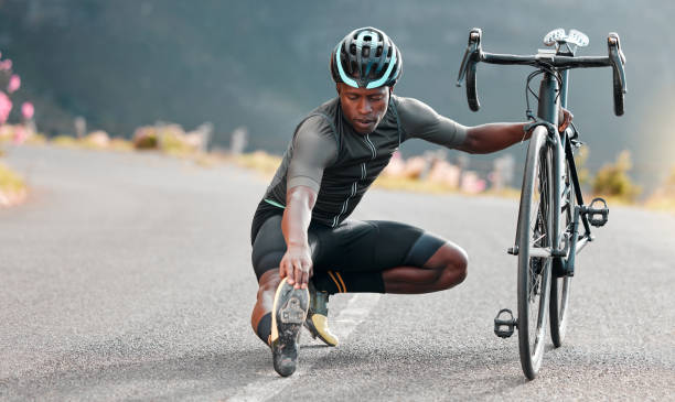 Outdoor, cycling and cyclist doing stretching exercise by his bicycle on road in mountain. Sports, training for fitness and man athlete doing warm up before cardio cycle workout with bike in nature. al aire libre, ciclismo y ciclista haciendo ejercicios de estiramiento con su bicicleta en carretera en montaña. deportes, entrenamiento para fitness y hombre atleta haciendo calentamiento antes del entrenamiento de ciclo cardiovascular con bicicleta en l