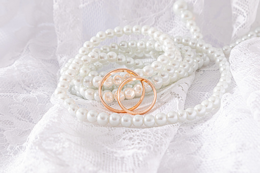 Retro beige tulle and long pearl beads hang along the soft folds of fabric with gold wedding rings. A copy space. mockup.