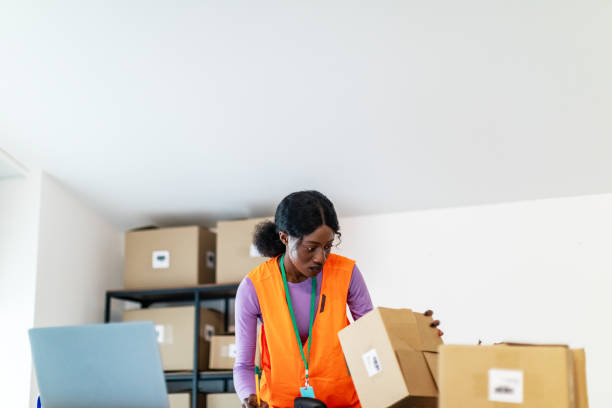 istock Young adult black woman ecommerce business worker scanning package using barcode reader at warehouse 1820228328