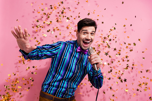 Photo of positive attractive guy hand hold wired microphone singing flying confetti christmas event isolated on pink color background