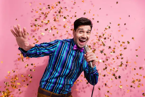 Photo of positive attractive guy hand hold wired microphone singing flying confetti christmas event isolated on pink color background.