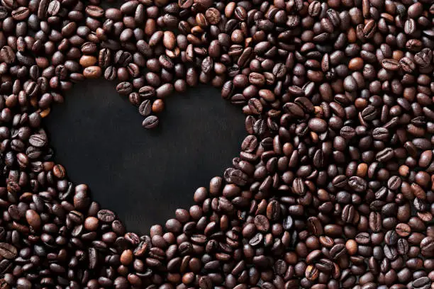 Photo of Coffee beans are laid out in the shape of a heart on a dark wooden surface