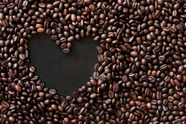 Photo of Coffee beans are laid out in the shape of a heart on a dark wooden surface