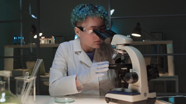 Female Researcher Studying Liquid under Microscope in Lab