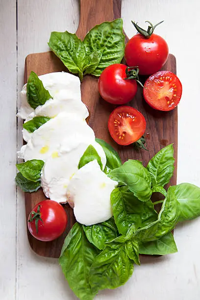 "A deconstructed salad of fresh tomatoes, basil leaves, and mozzarella cheese on a wood cutting board.View more of my"