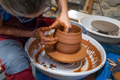 A woman working on the clay wheel creating a new piece stretching it with her hands.